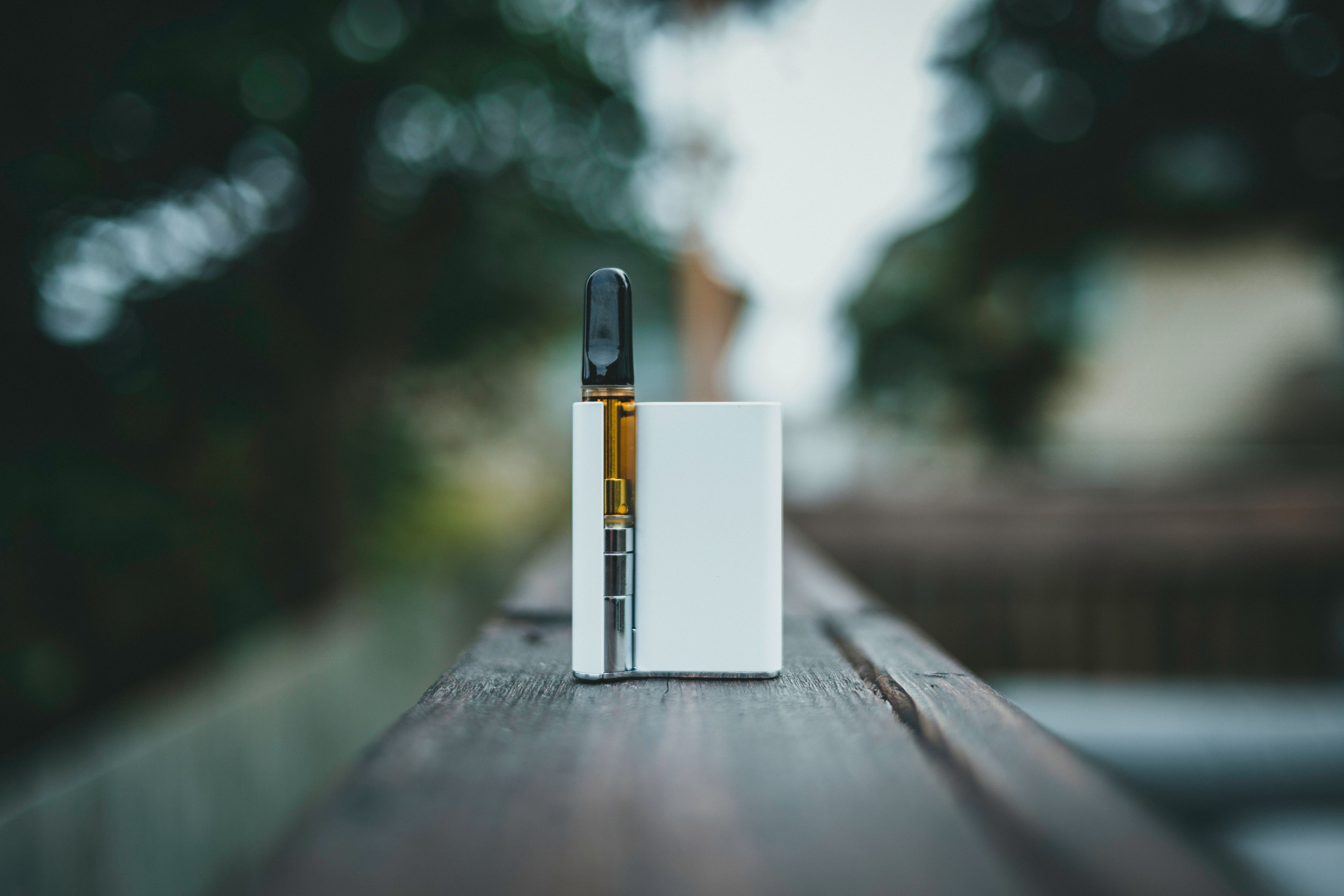 A white vape device sitting on a wooden surface outdoors